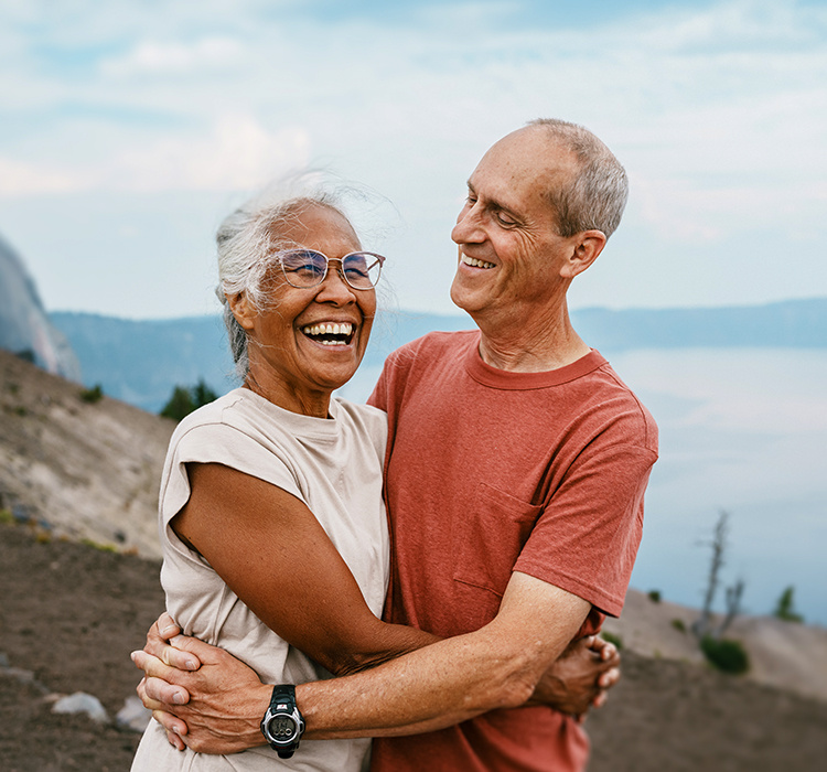 An older couple shares an embrace on a hike. 